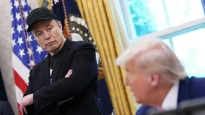 The image shows a person wearing a "DOGE" cap in a formal setting with an American flag in the background.