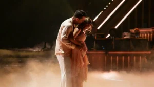 A couple shares an intimate moment on a stage with dramatic lighting and fog.