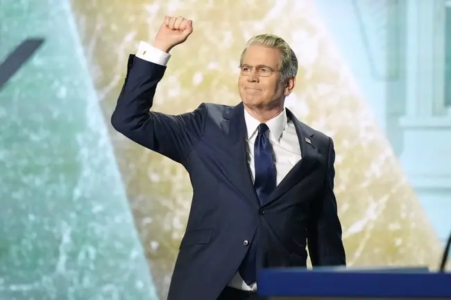 A man in a suit raises his fist in a gesture of triumph or solidarity on stage.