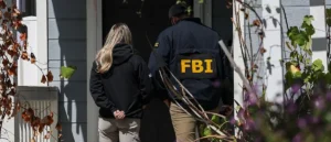 An FBI agent and a person in a black jacket are seen entering a house.