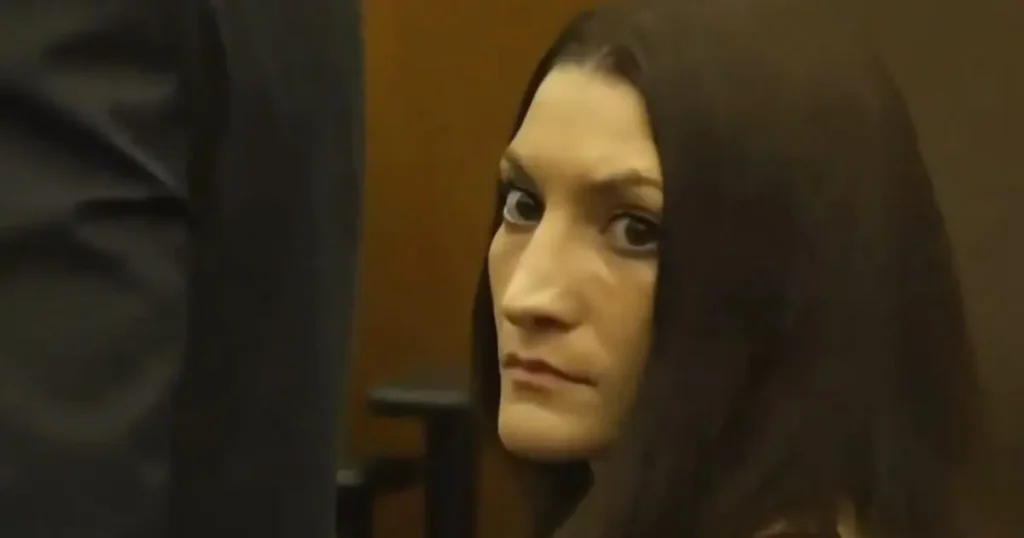 The image shows a person with long dark hair, wearing a dark garment, in what appears to be a courtroom setting.