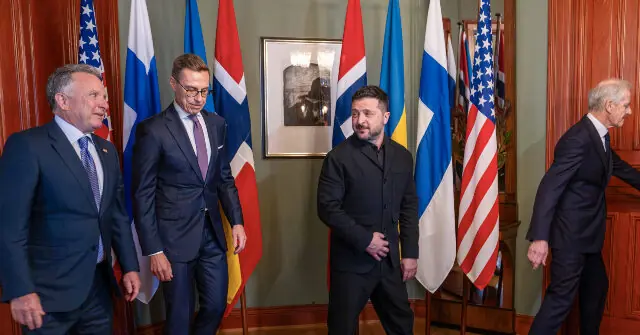 The photo shows a group of men in formal attire standing in front of various national flags, likely during a diplomatic or political meeting.
