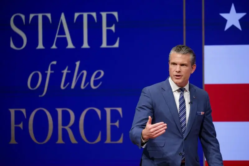 A man in a suit is giving a speech in front of a backdrop that reads "STATE of the FORCE" with an American flag design.