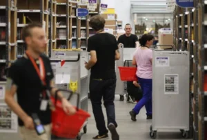 Employees are seen working in a warehouse, pushing carts and handling items, with shelves stocked in the background.