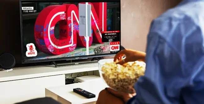A person enjoys a bowl of popcorn while watching CNN on a television.