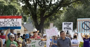 A group of people hold signs advocating against a proposed steel wall and protecting the environment in a protest.