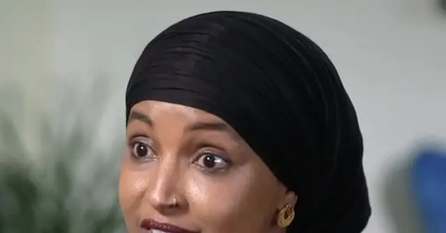 The image shows a person wearing a black headscarf and gold earrings, with a blurred background.