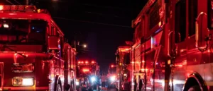 A nighttime scene shows multiple fire trucks with their lights on, indicating an emergency response.