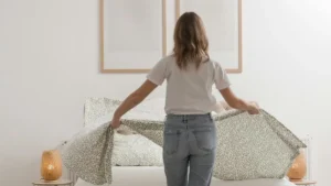 A person is making a bed with a patterned duvet in a minimalist bedroom setting.