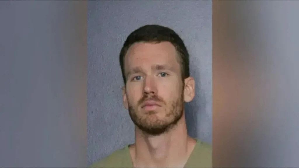 The image appears to be a mugshot of a man with short dark hair and a beard, wearing a light green shirt.