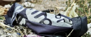 The image shows a discarded piece of fabric with a pattern lying among debris in a natural setting.
