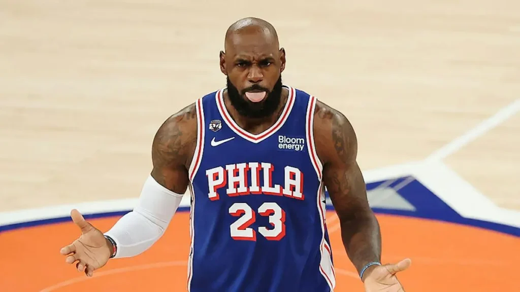 A basketball player wearing a Philadelphia 76ers jersey with the number 23 celebrates on the court.