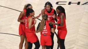 A group of basketball players in red uniforms huddle together on a court, possibly discussing strategy or celebrating a moment during a game.