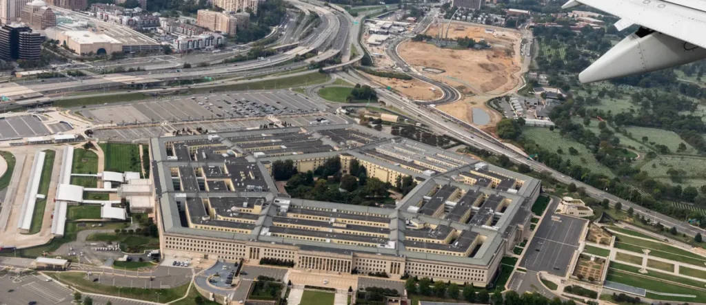 The image shows an aerial view of the Pentagon, the headquarters of the United States Department of Defense, surrounded by roads, parking lots, and green spaces.