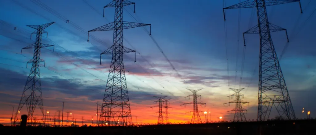 The image shows a silhouette of power transmission towers against a vibrant sunset sky, symbolizing the intersection of technology and nature.