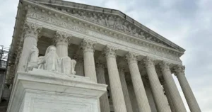 The image shows the exterior of the United States Supreme Court building, featuring its iconic columns and the statue of Justice in front.