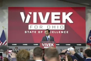 A man stands at a podium at a campaign rally for Vivek for Ohio, with a large banner in the background and an audience in the foreground.