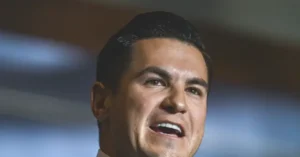 The image shows a close-up of a man speaking, with a focused and serious expression.