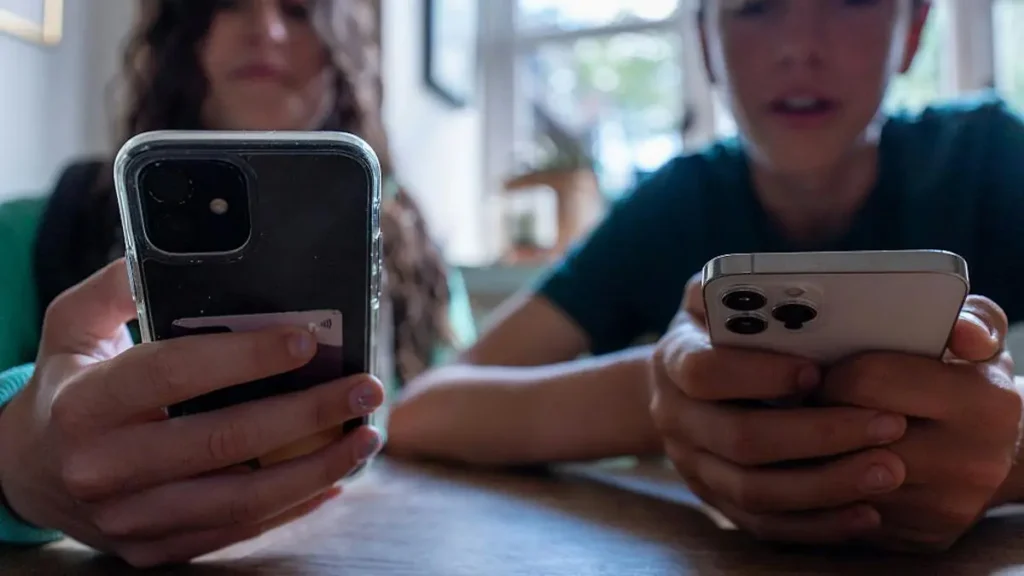 Two individuals are focused on their smartphones, highlighting the prevalence of digital engagement in modern life.