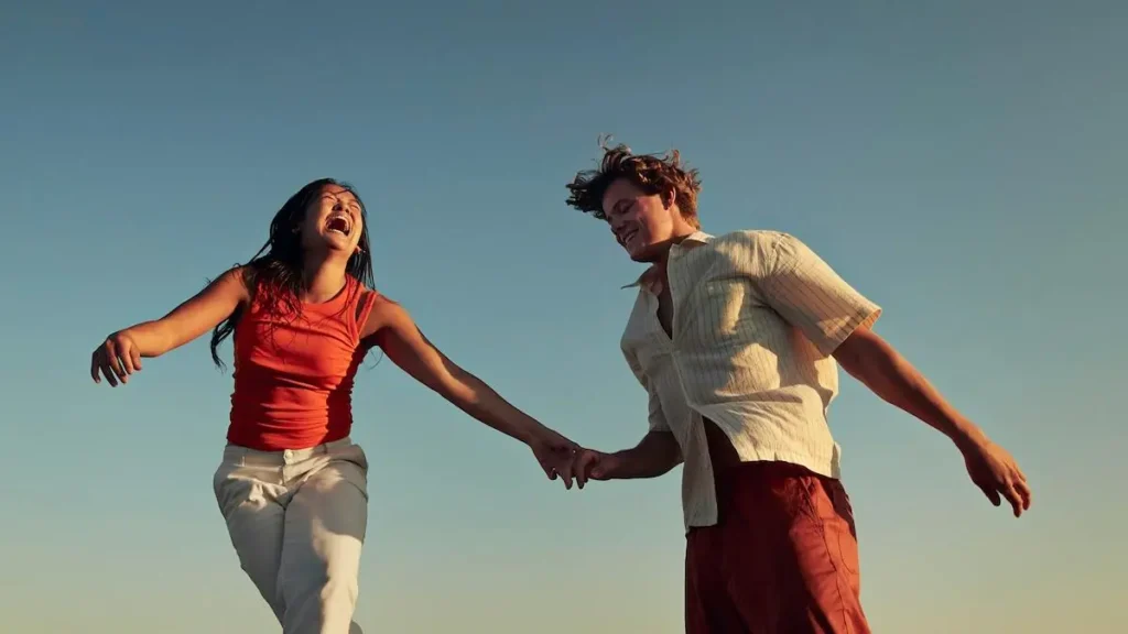 A couple is joyfully running hand in hand under a clear blue sky.