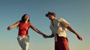 A couple is joyfully running hand in hand under a clear blue sky.