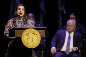 A woman stands at a podium adorned with the Great Seal of the State of Wyoming, delivering a speech at a formal event.