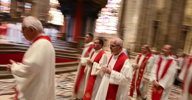 A group of clergy members in white robes with red stoles are standing in a grand cathedral, possibly during a religious service or ceremony.
