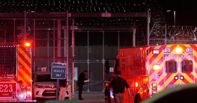 Emergency vehicles are parked outside a facility with barbed wire fencing at night.