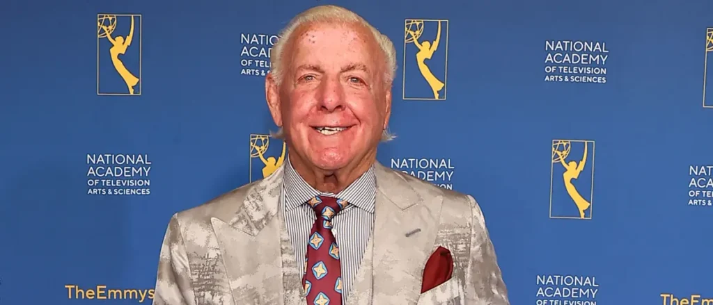 The image shows a man in formal attire standing in front of a backdrop featuring the National Academy of Television Arts & Sciences logo.