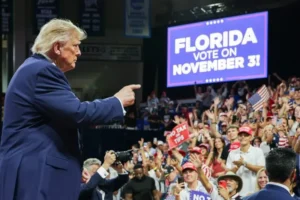 The image shows a political rally in Florida, with a crowd enthusiastically supporting a candidate who is pointing towards the audience.