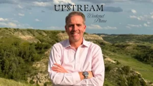 A man stands with his arms crossed in front of a scenic, hilly landscape under a partly cloudy sky, with the text "UPSTREAM Weekend Plans" overlaid.