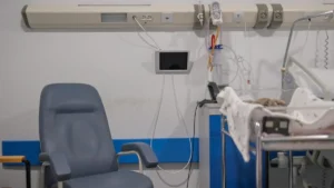 The image shows a hospital room with medical equipment, a chair, and a bed, indicating a healthcare setting.