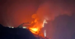 A large fire is burning intensely at night, with bright flames and thick smoke billowing into the sky.