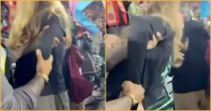 The image shows a person being restrained by others in a crowded setting, possibly during a protest or public event.