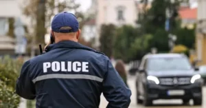 A police officer is seen from behind, wearing a uniform with "POLICE" written on the back, while holding a communication device.