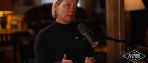 A woman is speaking into a microphone on a set resembling "The Tucker Carlson Show."