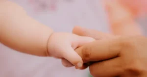 A close-up image captures a tender moment of a child's hand being held by an adult's hand, symbolizing care and connection.