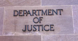 The image shows the engraved sign for the Department of Justice on a stone wall.