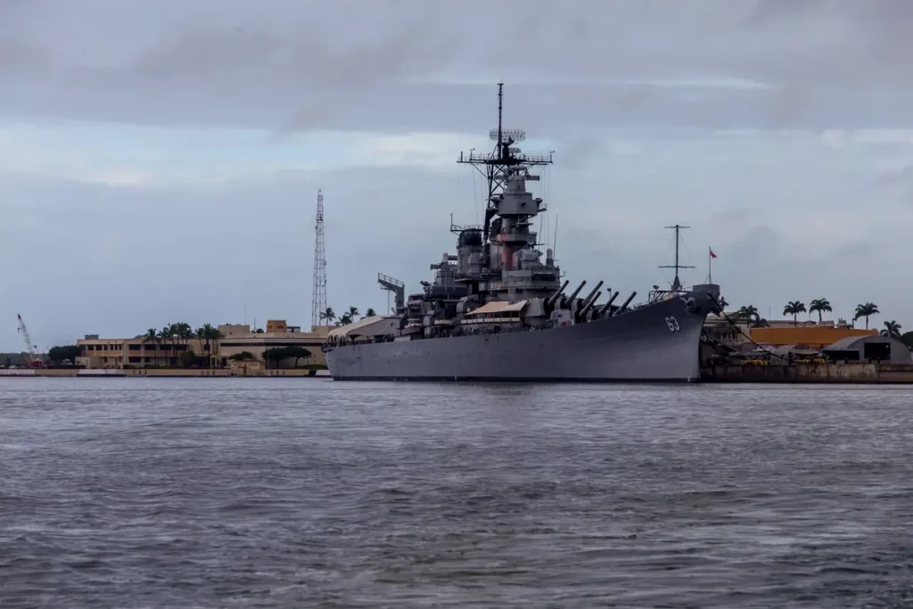 A battleship is docked in a harbor under a cloudy sky.