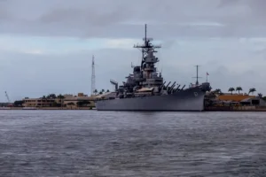 A battleship is docked in a harbor under a cloudy sky.
