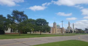 The image shows a serene view of a mosque and a church side by side, surrounded by greenery and a clear blue sky.