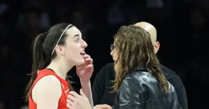 A basketball player in a red jersey is engaged in a conversation with a person in a black leather jacket.