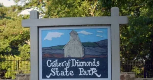 The sign for Crater of Diamonds State Park features a painted image of a barn and surrounding landscape.