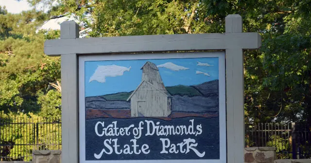 The sign for Crater of Diamonds State Park features a painted image of a barn and surrounding landscape.