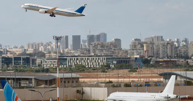 An airplane is captured in flight above a cityscape, with another plane on the ground at an airport.