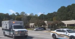 An ambulance and a sheriff's car are parked near a building with trees in the background.