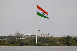 The Indian national flag waves prominently against a backdrop of urban buildings and greenery.