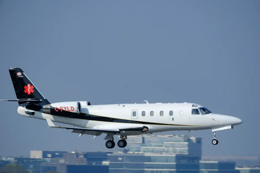 A medical aircraft with the registration C-FYLD is captured in flight, preparing to land against a backdrop of buildings.