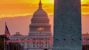 The image captures the iconic U.S. Capitol and Washington Monument at sunset, with American flags lining the foreground.