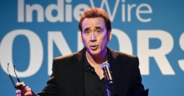A man is giving a speech at the IndieWire Honors event, holding a pair of glasses in one hand.